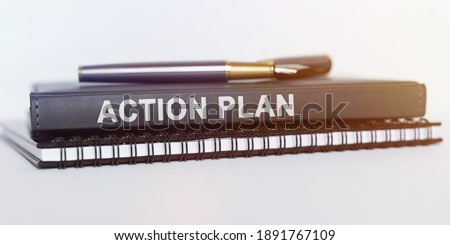 Business and education concept. On the table are a notebook, a pen and a book. The book says - ACTION PLAN