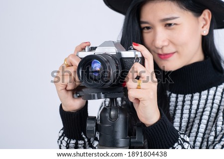 Portrait of female photographer holding a professional camera on tripod and taking images on grey background. Asian beautiful woman photography working in studio.
