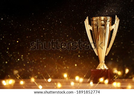 image of gold trophy over wooden table and dark background, with abstract shiny lights
