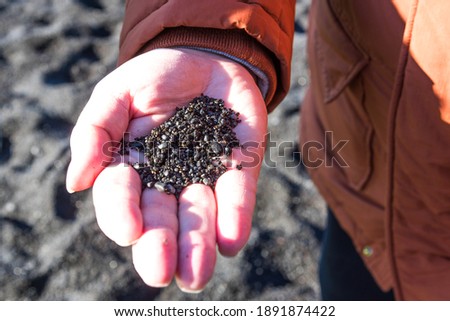 Black sand on the white man hand on the background of famous black sand beach Reynisfjara in Iceland. Close up black volcanic sand in man hand.