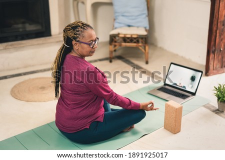 African senior woman doing yoga at home with laptop - Meditation, mindfulness and health care concept