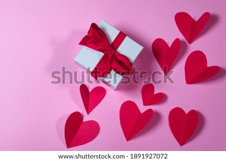 WHITE GIFT WITH RED RIBBON AND PAPER RED HEARTS ON PINK BACKGROUND
