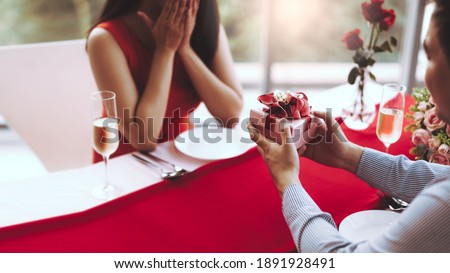 Valentine festive date at restaurant concept. Man couple hand hold a surprise romantic present red gift box give it to girlfriend. At hotel dinner table.