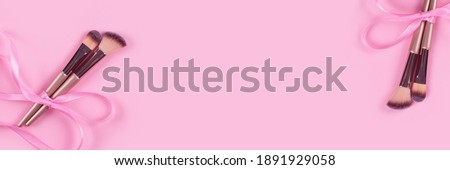 Banner with professional cosmetic makeup brush bounded with pink ribbon bow on light pink background with copy space for your text. Creative make-up concept. Selective focus