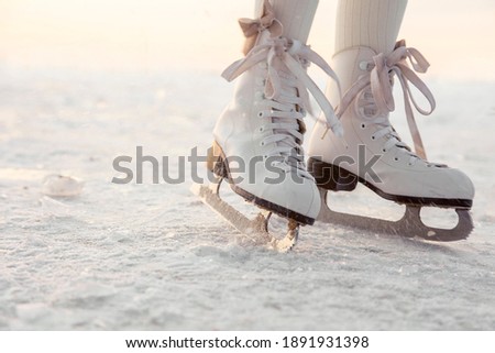 Legs of little girl skating on ice in evening sunset light. Winter sports on natural background
