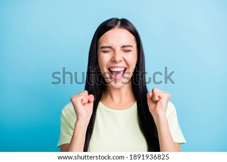 Photo portrait of cheerful woman with closed eyes celebrating with two fists up isolated on pastel blue colored background
