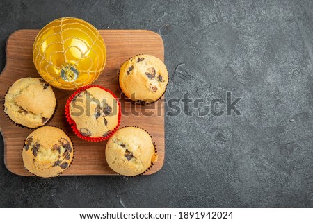 Half shot of freshly baked delicious small cupcakes with chocolates and accessory on wooden cutting board on the right side of dark background