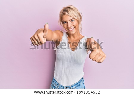 Young blonde girl wearing casual clothes approving doing positive gesture with hand, thumbs up smiling and happy for success. winner gesture. 