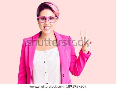 Young beautiful woman with pink hair wearing business jacket and glasses smiling with happy face winking at the camera doing victory sign. number two. 
