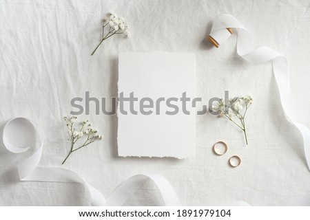 Wedding invitation card template. Top view blank paper card, ribbon, golden rings, flowers on white background. 