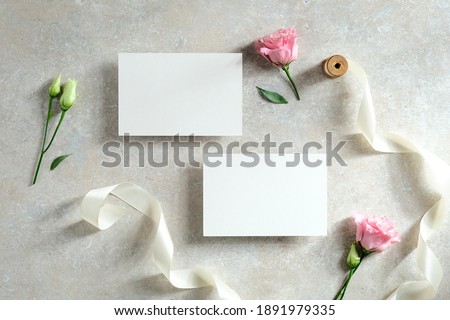 Blank paper cards, flowers, ribbon on stone table. Wedding invitation cards templates. Flat lay. Top view.