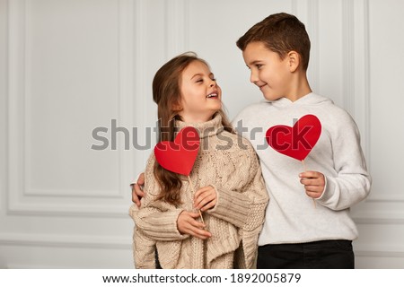 Happy couple little girl and boy with red hearts against white wall. smiling boy hugs girl. St. Valentine's Day