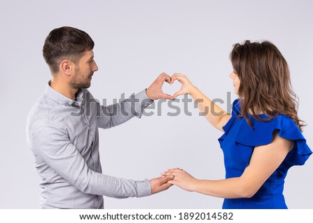 A loving couple holds hands and a heart shape on a gray background. St.Valentine's Day.