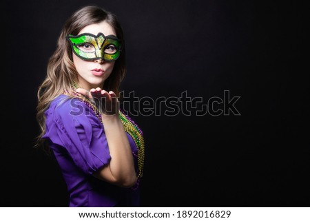 Mardi gras party, masquerade. Woman with a carnival mask and beads on the black background with copy space.
