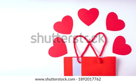 Online shopping concept. Red gift shopping bag, and red paper hearts isolated on white background, copy space, banner, flat lay. Background for Valentine's Day, Birthday, Mother's Day