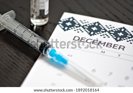 Syringe, vial and calendar with month of December on a black table ready to be used. Covid or Coronavirus vaccine background