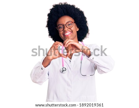 Young african american woman wearing doctor coat and stethoscope smiling in love doing heart symbol shape with hands. romantic concept. 