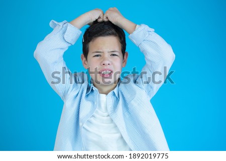 Young boy scratching his head isolated over blue background.