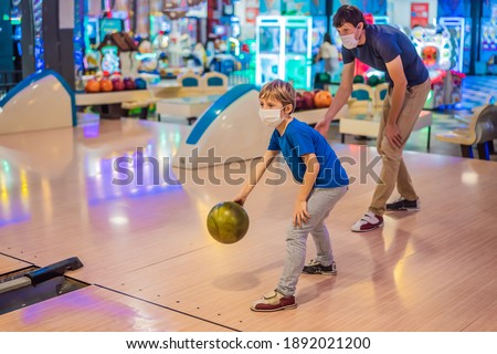 Father and son playing bowling with medical masks during COVID-19 coronavirus in bowling club