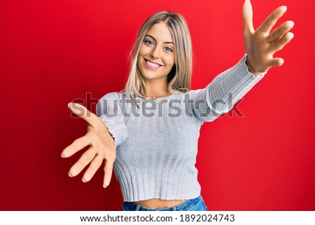 Beautiful blonde woman wearing casual clothes looking at the camera smiling with open arms for hug. cheerful expression embracing happiness. 