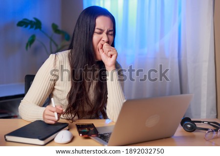 Young sleepy Asian woman sitting in front of computer yawning over worked at night, Asian female student  study online at night.  Royalty-Free Stock Photo #1892032750