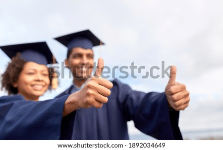 education, graduation, gesture and people concept - happy international graduate students in mortar boards and bachelor gowns outdoors showing thumbs up