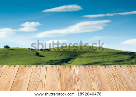 A Empty wooden table in front of a blurred background of a rural landscape of a meadow with cows. selective focus. space for copy and text. can be used to display or assemble your products.