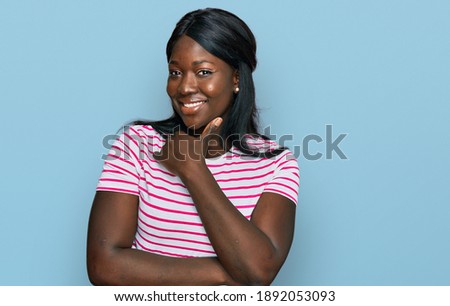 African young woman wearing casual striped t shirt looking confident at the camera smiling with crossed arms and hand raised on chin. thinking positive. 