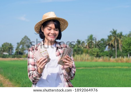 Asian farmer woman holding Thai banknote money with smile face at green rice farm