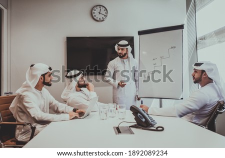 Cinematic image of an arabian group of people working in the office. Four men wearing traditional outfit from Dubai making business plans indoor