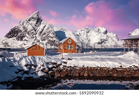 Amazing beautiful nature landscape  of Lofoten Islands. Amazing winter scenery with snow covered mountains pink colorful sky and tipical red fishing huts, rorbu during sunset. popular travel location  Royalty-Free Stock Photo #1892090932
