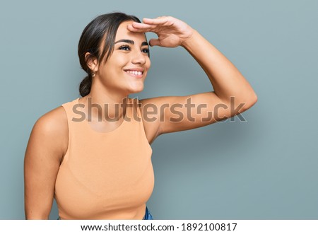 Young brunette woman wearing casual clothes very happy and smiling looking far away with hand over head. searching concept. 