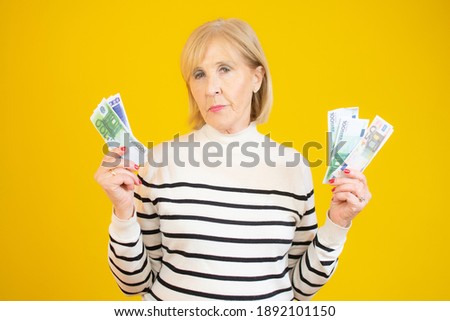 Cheerful Senior Woman Holding Money Banknotes over yellow background.