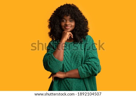 Smiling young beautiful black woman with booshie curly hair posing on yellow studio background, copy space. Happy and carefree african american young lady in green knitted sweater