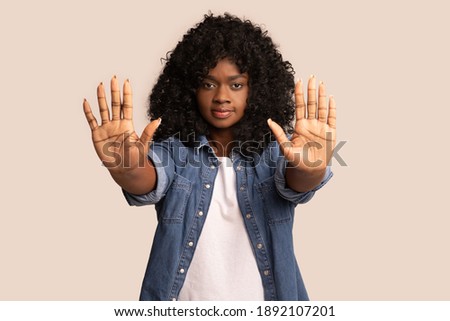 Irritated young black woman showing stop gesture with both palms over grey studio background, copy space. African american curly lady protesting against racism, sexism, violence, harrastment, abuse Royalty-Free Stock Photo #1892107201