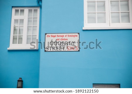 Address sign for Godfrey street on blue wall next to windows. Address sign on colorful British house from Chelsea, London. Peaceful London neighborhood