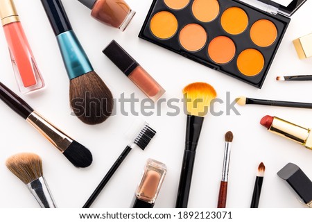 Plenty of makeup on the white table with eyelash brush, eye shadow, lipstick.