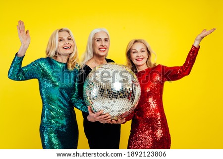 Beautiful senior woman making party and celebrating new year. Middle aged women wearing elegant glittering dresses and having fun. Studio portraits on colored background