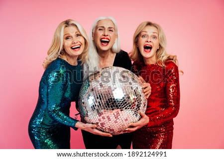 Beautiful senior woman making party and celebrating new year. Middle aged women wearing elegant glittering dresses and having fun. Studio portraits on colored background Royalty-Free Stock Photo #1892124991