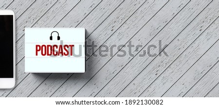 lightbox with message PODCAST and smartphone on wooden background