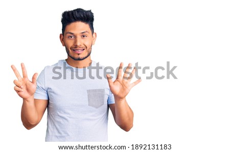 Handsome latin american young man wearing casual clothes showing and pointing up with fingers number eight while smiling confident and happy. 