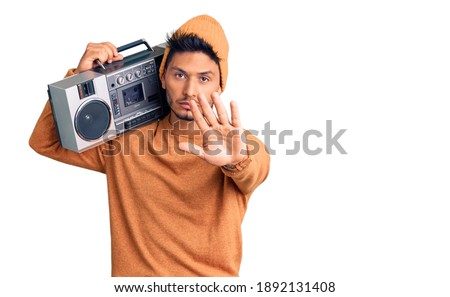 Handsome latin american young man holding boombox, listening to music doing stop sing with palm of the hand. warning expression with negative and serious gesture on the face. 