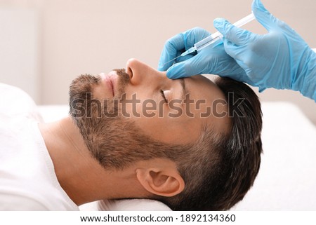 Side view of middle-aged man getting beauty injection in nose at aesthetic clinic. Plastic surgeon injecting anti-aging filler in handsome bearded man nose, having plastic correction, closeup Royalty-Free Stock Photo #1892134360