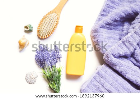 Orange shampoo package, purple lavender flowers, wooden comb and lilac towel. Flat lay photography natural organic hair care cosmetic products. Beauty still life photo