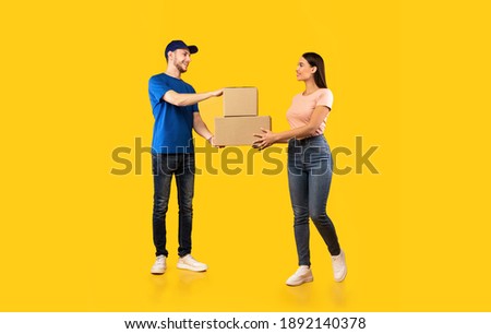 Parcel Delivery. Woman Receiving Boxes From Male Courier Standing Over Yellow Studio Background. Post Package Delivering And Transportation, Couriers Service Concept. Full Length Royalty-Free Stock Photo #1892140378