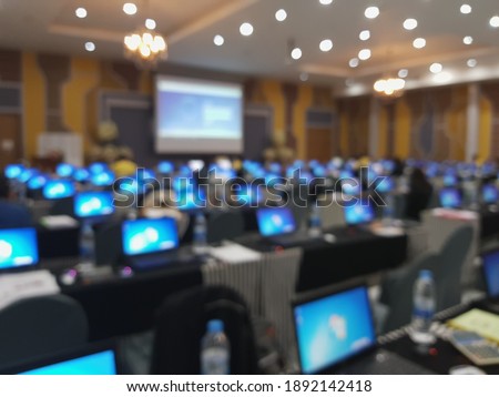 Blurred image of a large conference room with computers in use for meeting attendees.