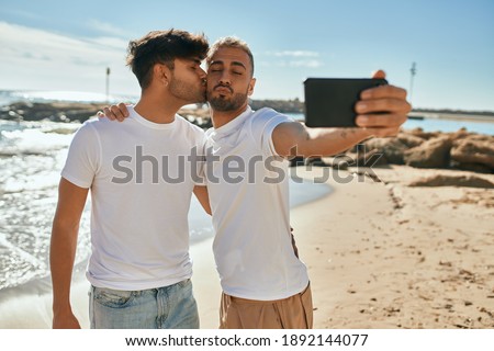 Young gay couple smiling happy making selfie by the smartphone at the beach.
