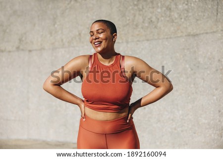 Plus size female model in sportswear smiling with her hands on hips. Positive woman relaxing after workout outdoors. Royalty-Free Stock Photo #1892160094
