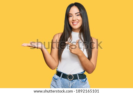 Young beautiful hispanic girl wearing casual clothes amazed and smiling to the camera while presenting with hand and pointing with finger. 