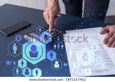 HR specialist researching and analyzing the data of salary on employment market to forecast ongoing expenses of the company using calculator. Hiring new talented officers. Social media hologram icons Royalty-Free Stock Photo #1892167462